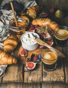 A European breakfast with croissants, coffee, and fruit.