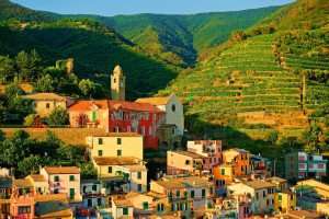 A typical village of Liguria, with a perched coastal town, brightly colored houses, and mountains behind.