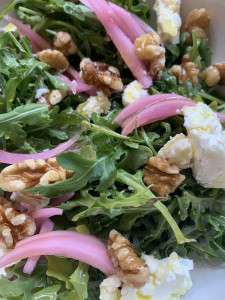 Closeup of a tasty arugula salad with pickled onions and walnuts.